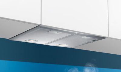 Unterbau-Dunstabzugshaube mit Beleuchtung vor blauem Hintergrund.